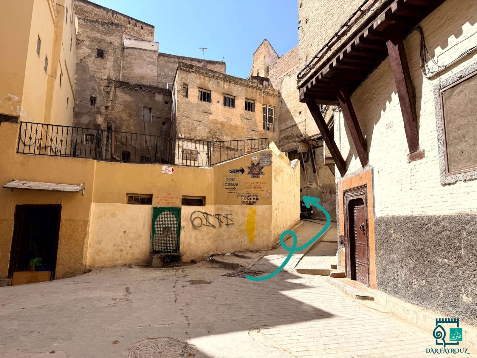 The small square with the green fountain; the lane climbs to the right of the yellow wall