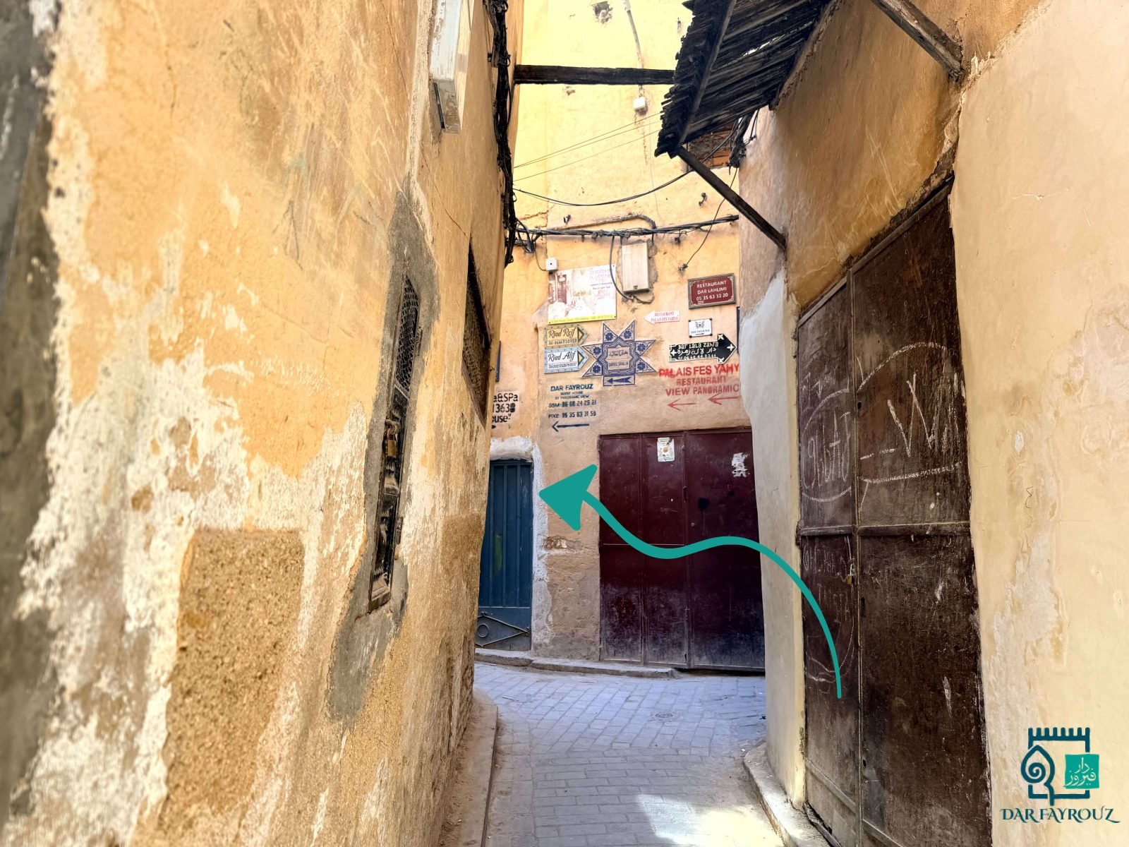 The narrow lane ending at a wall of signs; turn left by the teal door