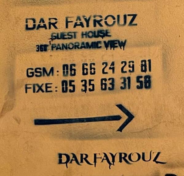 Dar Fayrouz stencil on the yellow wall by the fountain, arrow pointing right